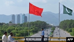 Seorang polisi berjaga di bawah bendera China dan Pakistan yang di pasang di sepanjang jalan menjelang kunjungan Wakil Perdana Menteri China He Lifeng, di Islamabad, Pakistan, 30 Juli 2023. (Foto: Farooq Naeem/AFP)
