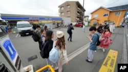 Tourists gather in front of the Lawson convenience store, a popular photo spot framing a picturesque view of Mt. Fuji in the background on cloudy evening of Tuesday, April 30, 2024, at Fujikawaguchiko town, central Japan.