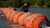 FILE - A kayaker walks past large buoys being used as a floating border barrier on the Rio Grande, Aug. 1, 2023, in Eagle Pass, Texas.
