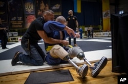 Vasyl Oksyntiuk, 26, right, a war veteran, receives help with the belt of his kimono during a Ukrainian national jiujitsu competition in Kyiv, Oct. 29, 2023. More than 20,000 people in Ukraine have lost limbs since the start of the Russian war.