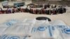 FILE - Somali people living in nearby camps queue in Mogadishu, Aug. 15, 2011, to receive cooked meals in the courtyard of a Somali no-governmental organization partnering with the World Food Program. 