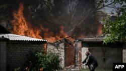 Mwanamke akiondoka katika nyumba inayoungua moto baada ya kupigwa bomu na wanajeshi wa Russia katika mji wa Lysytsansk mashariki mwa Ukrain. May 30, 2022