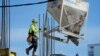 A worker guides a bin into position at a construction site, Jan. 24, 2023, in Miami.