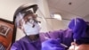 Dentist Dr. Kathleen Saturay wears additional protective equipment, including a face shield and disposable mask over a respirator mask, as she exams a patient in Seattle, May 27, 2020.