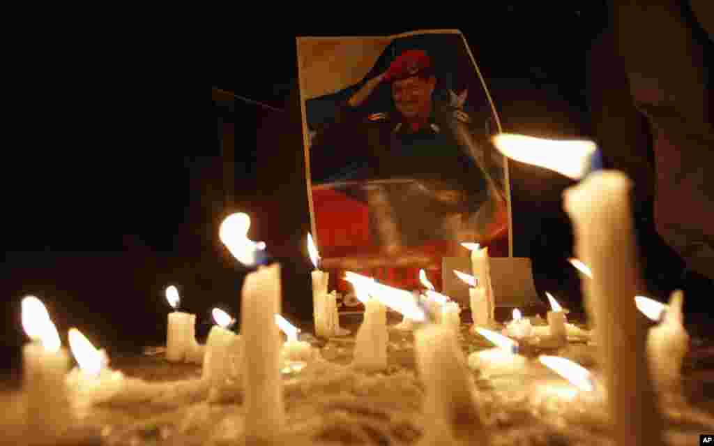 Candles, placed by mourner demonstrators, burn in front of an image of Venezuelan President Hugo Chavez outside Venezuela's embassy in Quito, Ecuador, March 5, 2013.