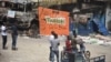 Des gens se tiennent près d'un mur d'une boutique endommagée qui dit: "non à la violence, Toumodi est la base" sur le marché de Toumodi le 4 novembre 2020.