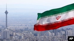 FILE - Iran's national flag flutters in the wind as the Milad telecommunications tower and buildings are seen in the background, in Tehran, Iran, March 31, 2020. 