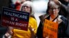 Jo Ann Waker-Ferrand, left, and Jan Miller, both of Denver, wave their placards during a protest, June 23, 2017, in downtown Denver, against the Republican health bill that was recently unveiled in the U.S. Senate.