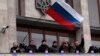 FILE - In this March 5, 2014 file photo, pro-Russia demonstrators holding a Russian flag, with the Ukrainian emblem in the background, stand on the balcony of the regional administrative building after storming it in Donetsk, Ukraine