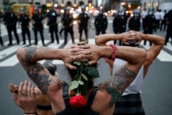 FILE - Protesters kneel in front of New York City Police Department officers before being arrested for violating curfew beside the iconic Plaza Hotel on 59th Street, in New York, June 3, 2020.