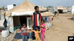 Syrian refugees stand near their tent at Kawergost refugee camp in Irbil, 217 miles (350 kilometers) north of Baghdad, Iraq, Sept. 22, 2013. 