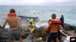 People clamber on the rocky shore on Christmas Island during a rescue attempt as a boat breaks up in the background, December 16, 2010