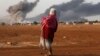 Syrian Kurd Kiymet Ergun, 56, standing in Mursitpinar on the outskirts of Suruc, at the Turkey-Syria border, watches while thick smoke rises following an airstrike by the US-led coalition in Kobani, Oct. 13, 2014.