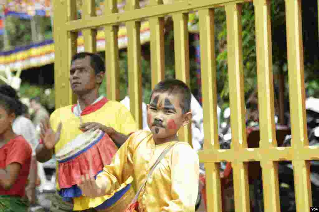 កុមារាម្នាក់កំពុងវាយស្គរនៅខាងមុខក្លោងទ្វារមាត់ដើម្បីស្វាគមន៍ពុទ្ធបរិស័ទដែលអញ្ជើញមកវត្តមួយកណ្តាលរាជធានីភ្នំពេញកាលពីព្រឹកថ្ងៃសៅរ៍ ទី១៦ ខែ កញ្ញា ឆ្នាំ២០១៧។(ទុំ ម្លិះ/VOA)