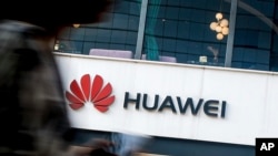 FILE - A woman walks by a Huawei retail store in Beijing, July 30, 2019. 