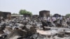 Mutane suna tsaye a inda mayakan Boko Haram suka kai hari a garin Gambaru, na jihar Barno, May 11, 2014.