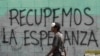 FILE - A man with a misplaced face mask walks past graffiti on a wall that reads in Spanish "Let's get hope back," in Caracas, Venezuela, March 29, 2020.