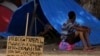 En esta foto del 11 de marzo del 2018, un cartel que dice 'necesito trabajo. Conductor de tractores. Excavador', cerca a un migrante venezolano que descansa fuera de su tienda de camapaña en la plaza Simón Bolívar, donde los venezolanos se han instalado en Boa Vista, Roraima, Brasil. 