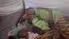 FILE - Two children and their mother rest under a mosquito net in the small village of Walikale, Congo.