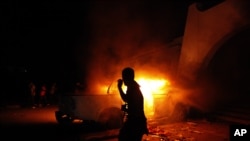 FILE - A Libyan civilian watches one of Ansar al-Shariah Brigades cars on fire, after hundreds of Libyans, Libyan Military, and Police raided the Brigades base, in Benghazi, Libya, Sept. 21, 2012. 