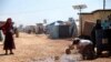 FILE - A refugee is seen scooping water from a puddle at a camp on the Syrian side of the border with Turkey, near the town of Atma, in Idlib province, Syria, April 19, 2020.