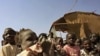 In this photo of Thursday, Jan.12, 2012 a mother waits with her son for emergency food rations from the World Food Program in the town of Gumuruk, 35 kilometers southwest of Pibor, South Sudan. Tens of thousands fled their homes after ethnic violence erup