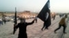 A fighter of the Islamic State of Iraq and the Levant (ISIL) holds an ISIL flag and a weapon on a street in the city of Mosul, June 23, 2014.