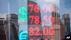 skyscrapers of the "Moscow City" are reflected in a glass window of an exchange office with the screen shows the currency exchange rate of the Russian ruble and U.S. dollar, Euro in Moscow, Russia, Tuesday, April 21, 2020. The Russian ruble fell Tuesday, driven down by a drop in oil prices. (Andrei Nikerichev, Moscow News Agency photo via AP)