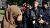 A woman wearing a full-face veil, or niqab, covers her eyes as she stands near police in Lille, France, in this September 22, 2012, file photo.