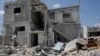 FILE - Saher al-Ali's family members stand inside their damaged house in the rebel-held town of Nairab, Idlib region, Syria, April 17, 2020. 