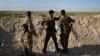 FILE - Fighters from the U.S-backed Syrian Manbij Military Council stand behind a sand barrier as they look toward a Turkish-backed fighters' position at the front line of Halawanji village, north of Manbij town, Syria, March 29, 2018. 