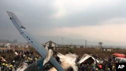 FILE - In this March 12, 2018, file photo, Nepalese rescuers stand near a passenger plane from Bangladesh that crashed at the airport in Kathmandu, Nepal. An investigation report released Monday, Jan. 28, 2019, says the pilot of the Bangladeshi airliner was disoriented and had lost situational awareness before his plane crashed in Nepal last year, killed 51 people and injuring 20. (AP Photo/Niranjan Shreshta, File)