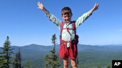 In this July 23, 2021 family photograph provided by Joshua Sutton, five-year-old Harvey Sutton raises his arms on a mountain top in Bigelow Preserve, Maine, while hiking the Appalachian Trail with his Mom and Dad.